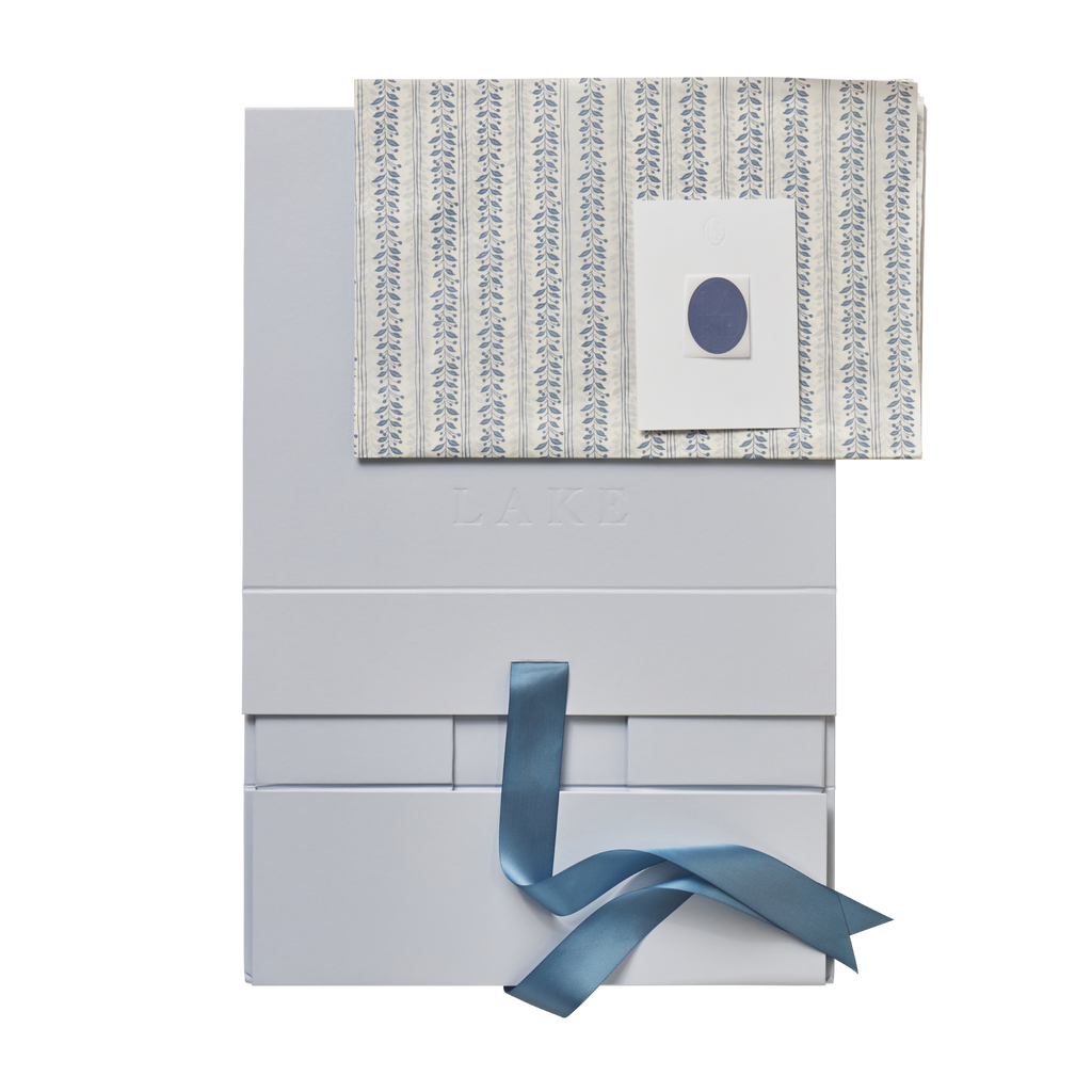 Flat white self-assemble box with leaf-patterned lid, circular window, and blue ribbon tie.