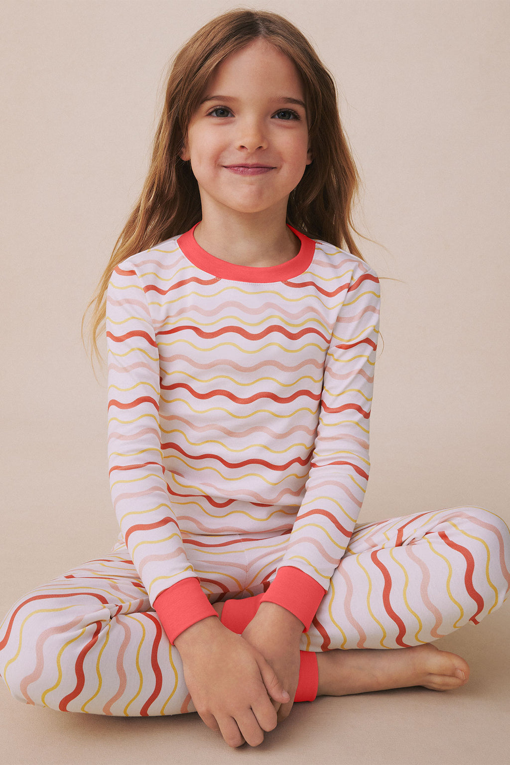 Child wearing long-sleeve top and pants with wavy horizontal stripes in red, yellow, and pink on white background.