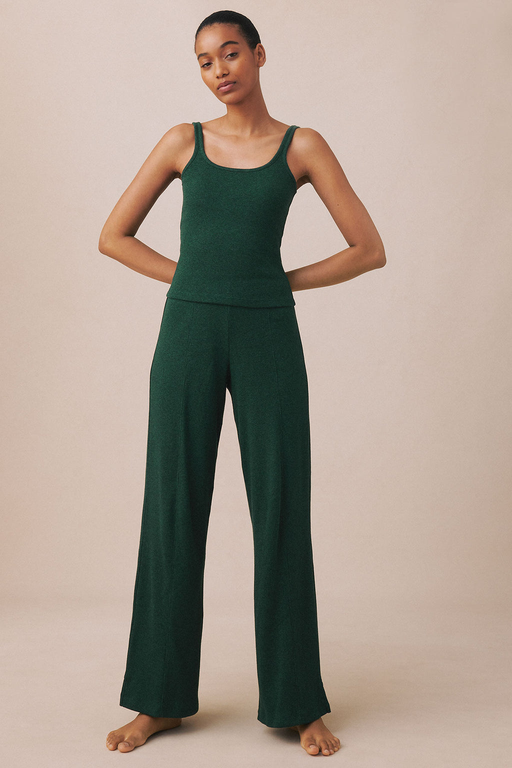 Woman wearing trekking green heather ribbed tank top and wide-leg pants, standing barefoot against neutral background.