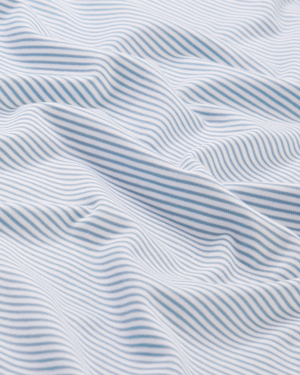 Close-up of the Mens Pima Sleep Bundle in Anchor Blue: white fabric with thin light blue stripes, gentle folds, and 100% Pima cotton for a soft texture and sense of movement.