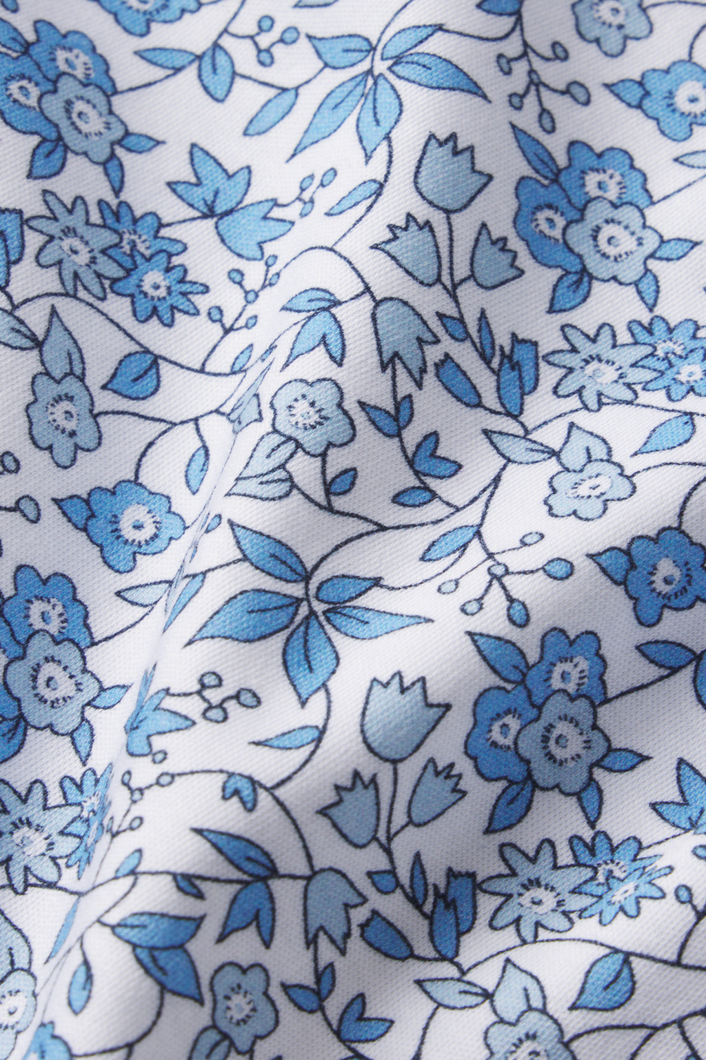 The Pima Crew Long Sleeve Bundle in Delft Blue Garden Floral features white fabric with blue floral patterns in small and medium sizes. Made from 100% Pima cotton, it offers subtle shadows and texture for an elegant look.