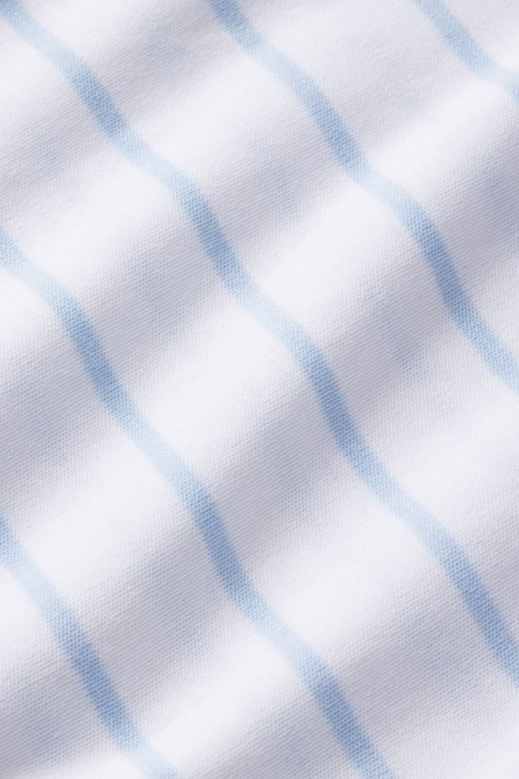 Close-up of white fabric from the Pima Long-Short Set in Marine, crafted from 100% Pima Cotton with a soft grid of light blue Breton stripes; the material appears smooth with a subtle texture.