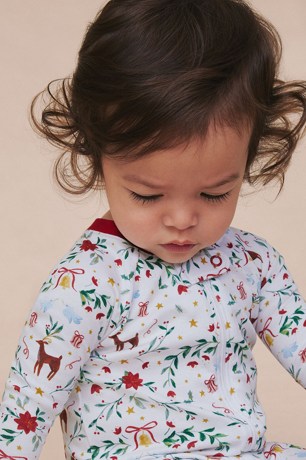 Baby sleeper with red collar featuring holiday-themed print including reindeer, poinsettias, stars, and bows on light backgro