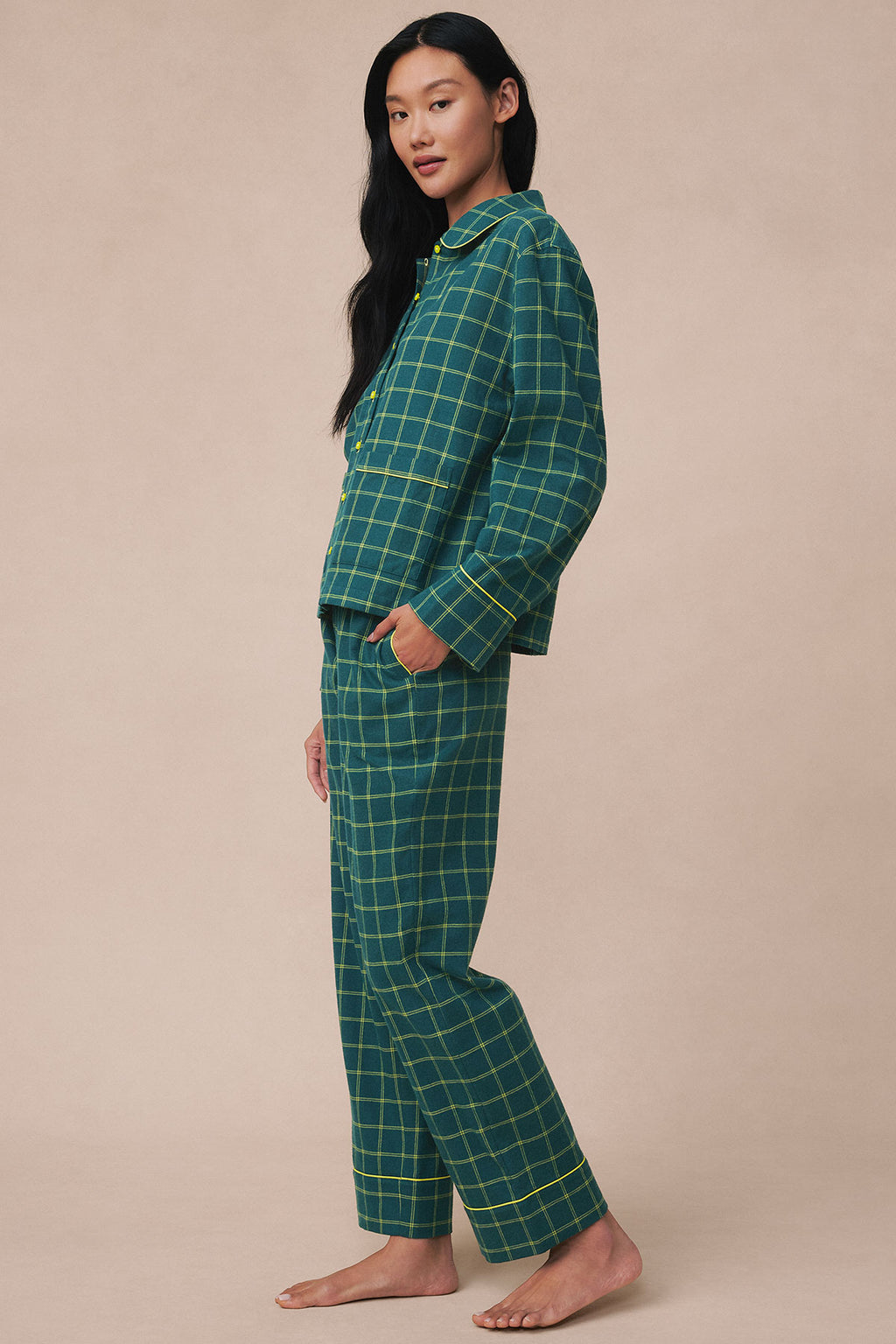 Woman wearing dark teal flannel pajama set with yellow windowpane plaid pattern, consisting of button-up shirt and matching p