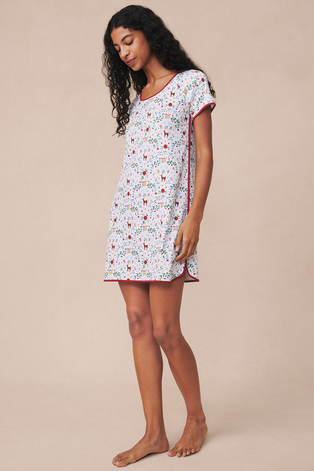 Woman wearing white nightgown with red and green holiday print, short sleeves, and red trim at neckline and hem.