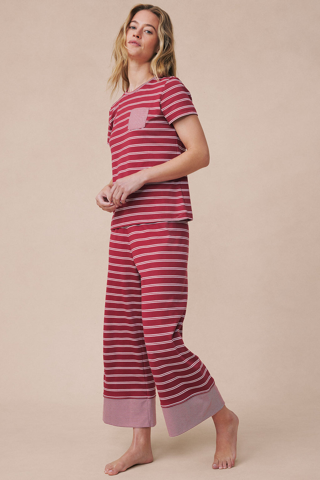 Woman wearing garnet and white striped crew neck short-sleeve pajama top with matching wide-leg cropped pants.