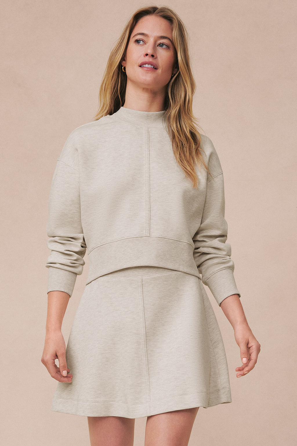 Woman wearing oat heather crew neck sweatshirt and matching mini skirt with ribbed waistband.