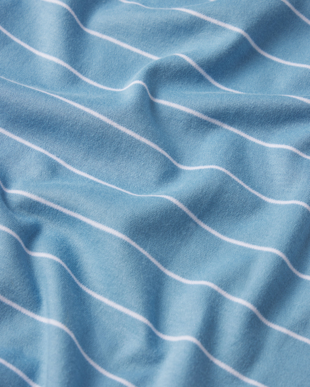 The Pima Ruffle Nightgown in Serene Blue Boating Stripe features light blue fabric with thin white stripes, subtle folds, and is crafted from soft Pima cotton.