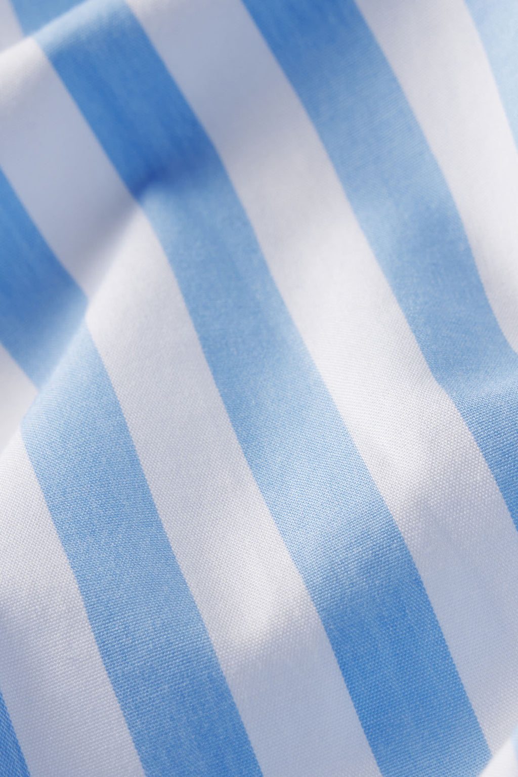 Close-up of 100% cotton fabric in Baltic Blue Beam Stripe, featuring soft light blue and white vertical stripes with gentle folds. Adds texture to the Poplin Piped Short-Long Set.