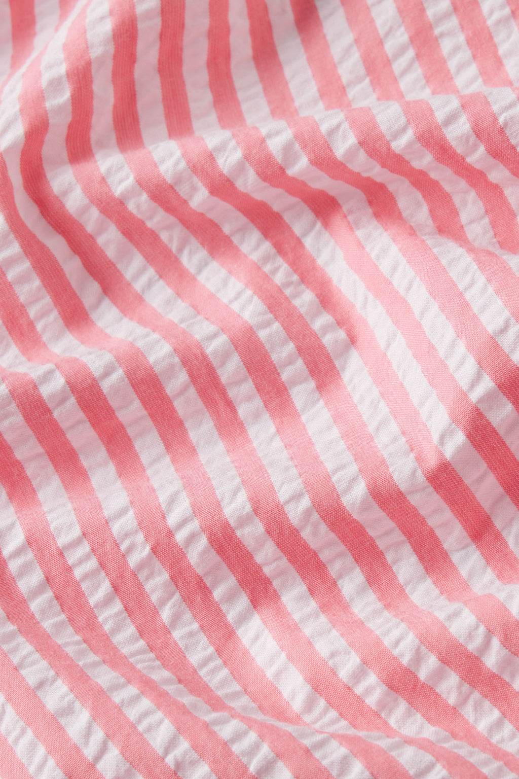 A close-up of the Alice Shorts Set in Gelato Seersucker shows its soft pink and white, gently wrinkled texture. Crafted from luxurious Pima cotton.