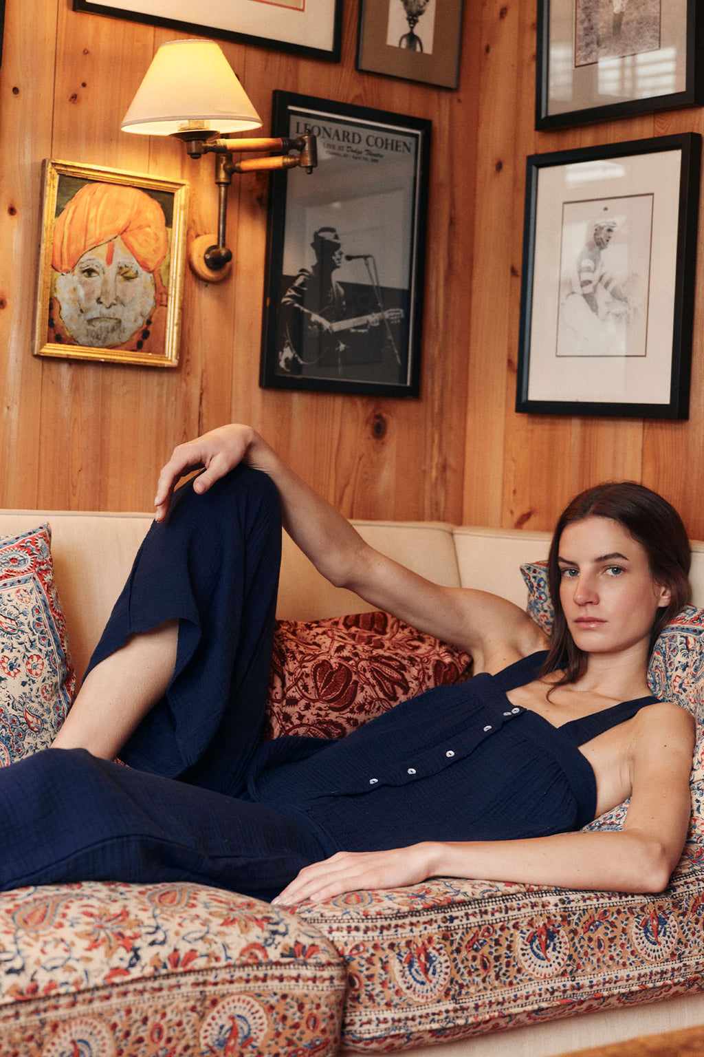 Woman wearing navy gauze button-up shirt and matching wide-leg pants, reclining on patterned sofa.