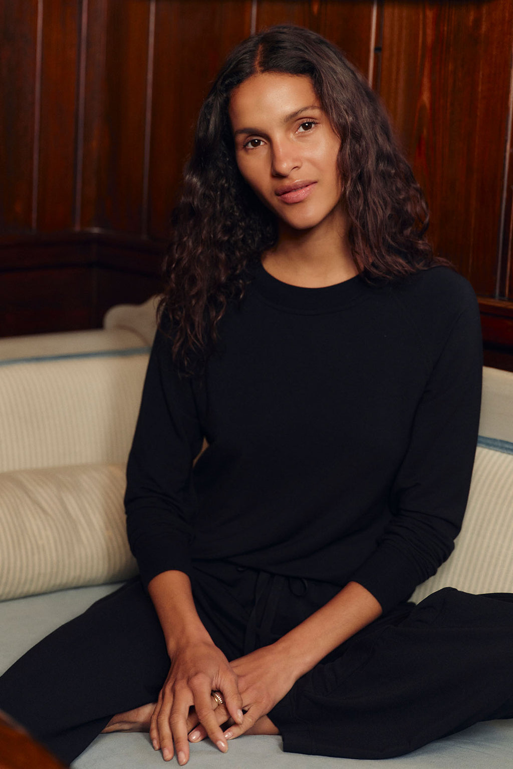 Woman wearing black long-sleeve top and black pants sitting on a cream-colored sofa.