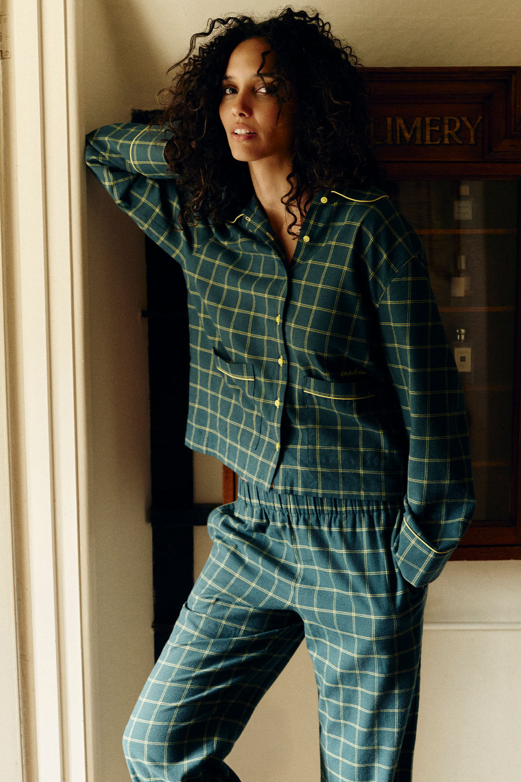 Woman wearing dark teal and yellow windowpane flannel pajama set with button-up shirt and matching pants.