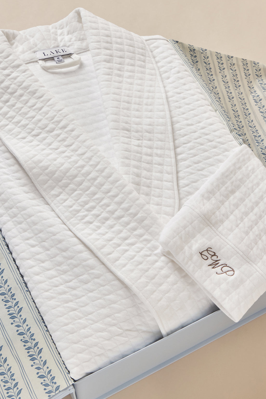 White quilted spa robe with long sleeves and embroidered cuff detail, displayed folded in box.